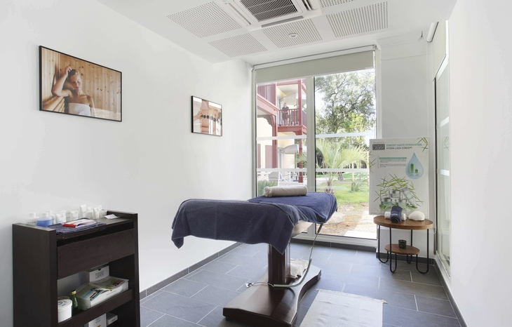 Ein heller Wellnessraum mit Massageliege und großen Fenstern.