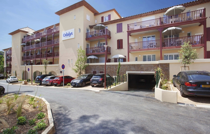 Fassade der Odalys Résidence Prestige Les Canissons mit geparkten Autos davor.