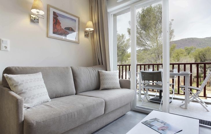 Wohnzimmer mit Sofa, Tisch, Balkon und Ausblick auf Bäume und Hügel in Cavalaire-sur-Mer.