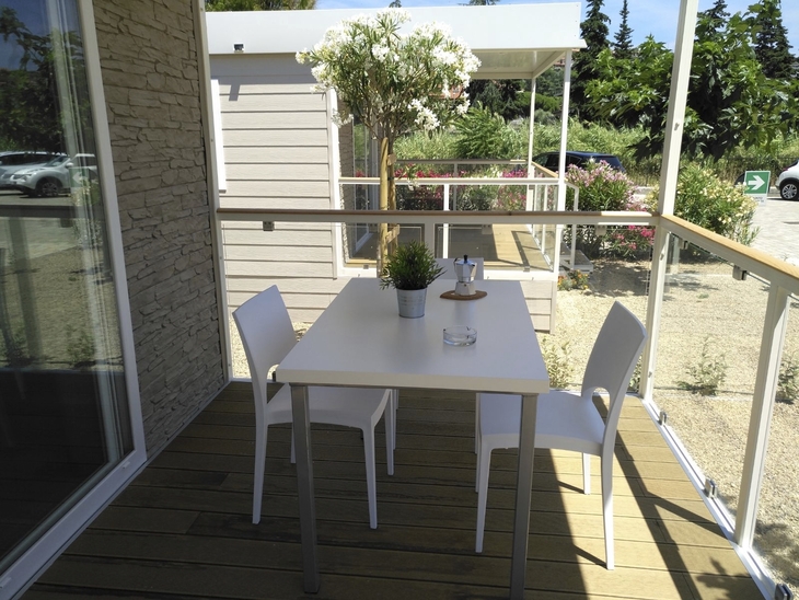 Terrasse mit Tisch, zwei Stühlen und Pflanzen, Blick auf Mobilheim und Garten.