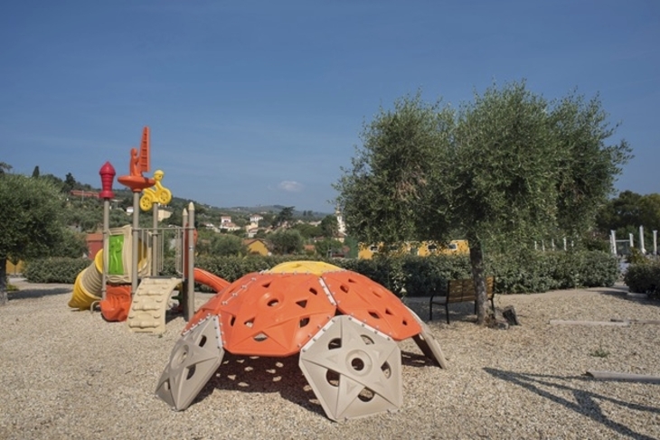 Spielplatz mit Klettergerüst und Rutsche, umgeben von Bäumen und Landschaft.