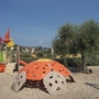 Spielplatz mit Klettergerüst und Rutsche, umgeben von Bäumen und Landschaft.