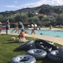Kinder spielen im Schwimmbad in einer grünen Anlage mit Reifen und Hügel im Hintergrund.