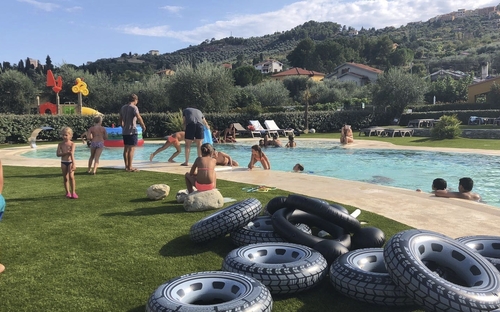 Kinder spielen im Schwimmbad in einer grünen Anlage mit Reifen und Hügel im Hintergrund.