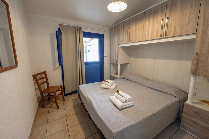 Schlafzimmer mit Doppelbett, weißer Bettwäsche, Holzstuhl und Fenster.