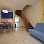 Wohnbereich mit blauer Couch, Esstisch, Küche und Holztreppe in modernem Apartment.