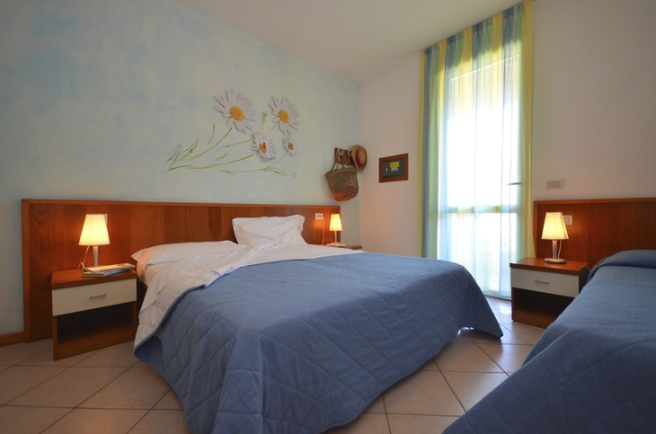 Hotelzimmer mit zwei Lampen, blauen Bettdecken und Blumenbild an der Wand.