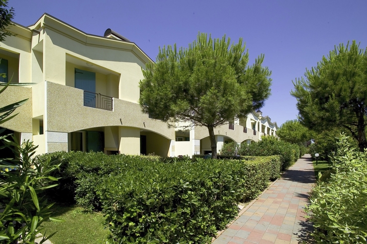 Gepflegte Apartmentanlagen mit Gartenweg und Bäumen unter blauem Himmel.