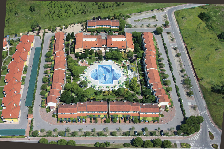 Luftaufnahme eines Ferienresorts mit Pool im Zentrum und roten Dächern in Bibione.