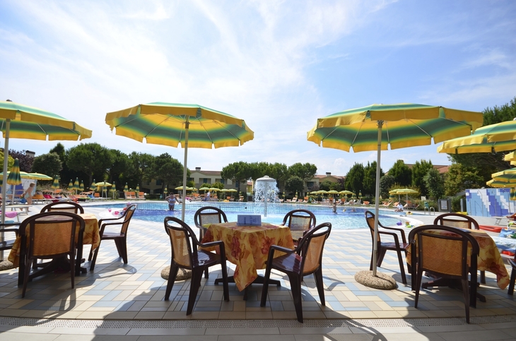 Tische mit gelben Sonnenschirmen an einem Pool an einem sonnigen Tag.