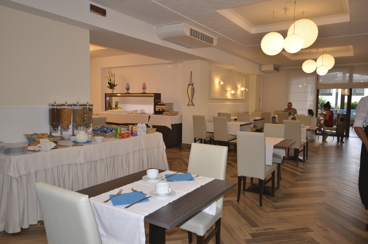 Innenansicht des Frühstücksraums im Hotel mit gedeckten Tischen und Buffet.