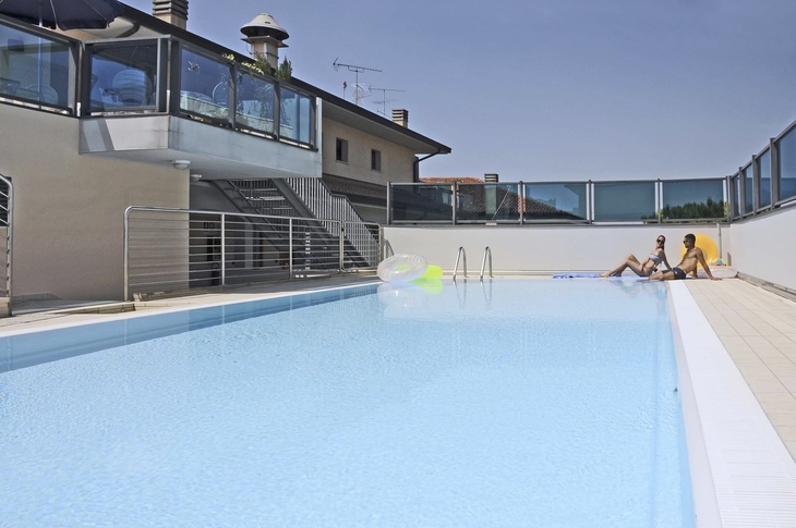 Hotelpool mit Liegestühlen und Sonnenschirmen, im Hintergrund ein Gebäude.