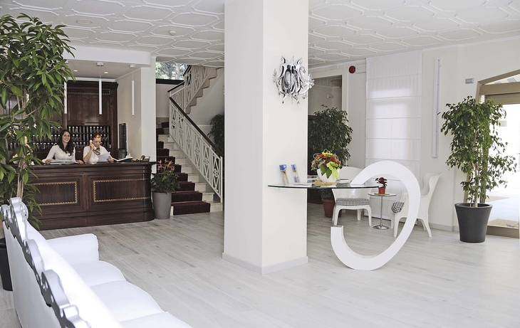 Helle Hotel-Lobby mit Rezeption, Pflanzen und Sitzbereich.