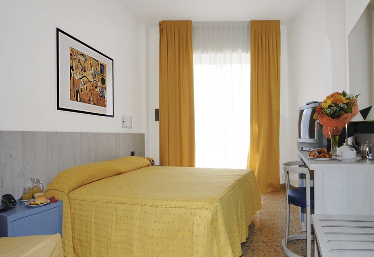 Modernes Hotelzimmer mit gelbem Bett und Vorhängen, Schreibtisch und Fernseher.