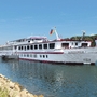 Kreuzfahrtschiff auf einem Fluss bei klarem Himmel und bewaldetem Ufer.