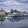 Ein Flusskreuzfahrtschiff nahe eines Schlosses auf einem ruhigen Fluss.