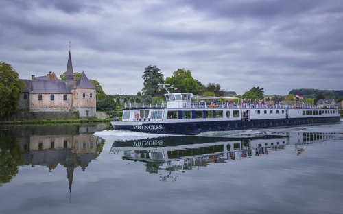 Ein Flusskreuzfahrtschiff nahe eines Schlosses auf einem ruhigen Fluss.