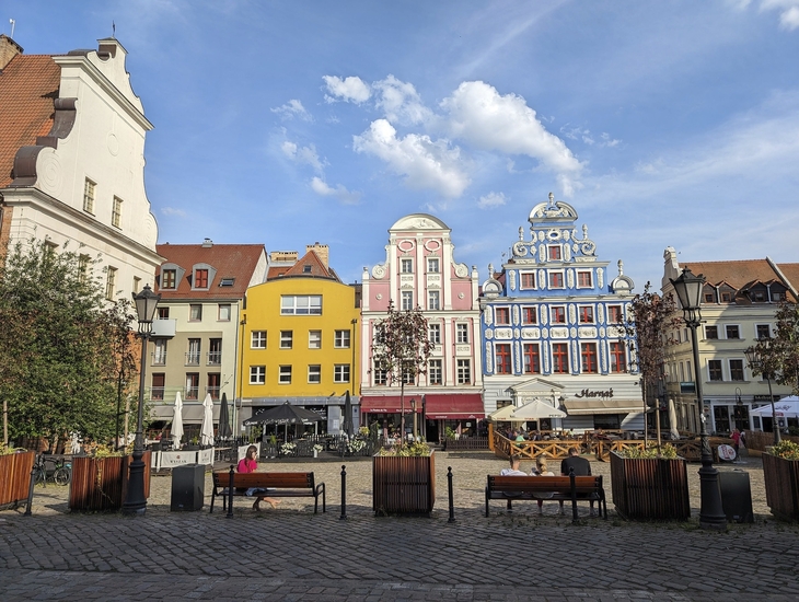 Bunter Marktplatz mit historischen Gebäuden und Himmel mit Wolken.