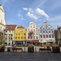 Bunter Marktplatz mit historischen Gebäuden und Himmel mit Wolken.