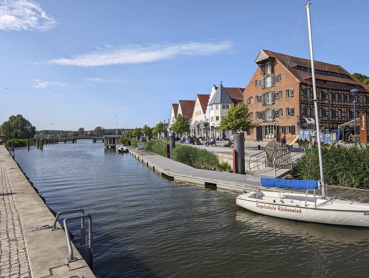 Hafenpromenade von Wolgast mit Segelboot und historischen Gebäuden bei Sonnenschein.