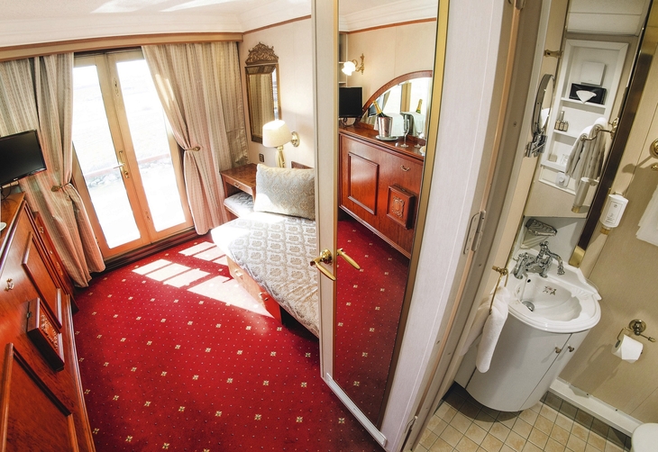 Kompakte Kabine mit rotem Teppich und kleinem Badezimmer auf einem Schiff.
