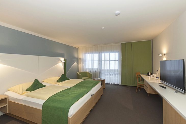 Modern eingerichtetes Doppelzimmer mit großem Fenster und grünem Dekor.