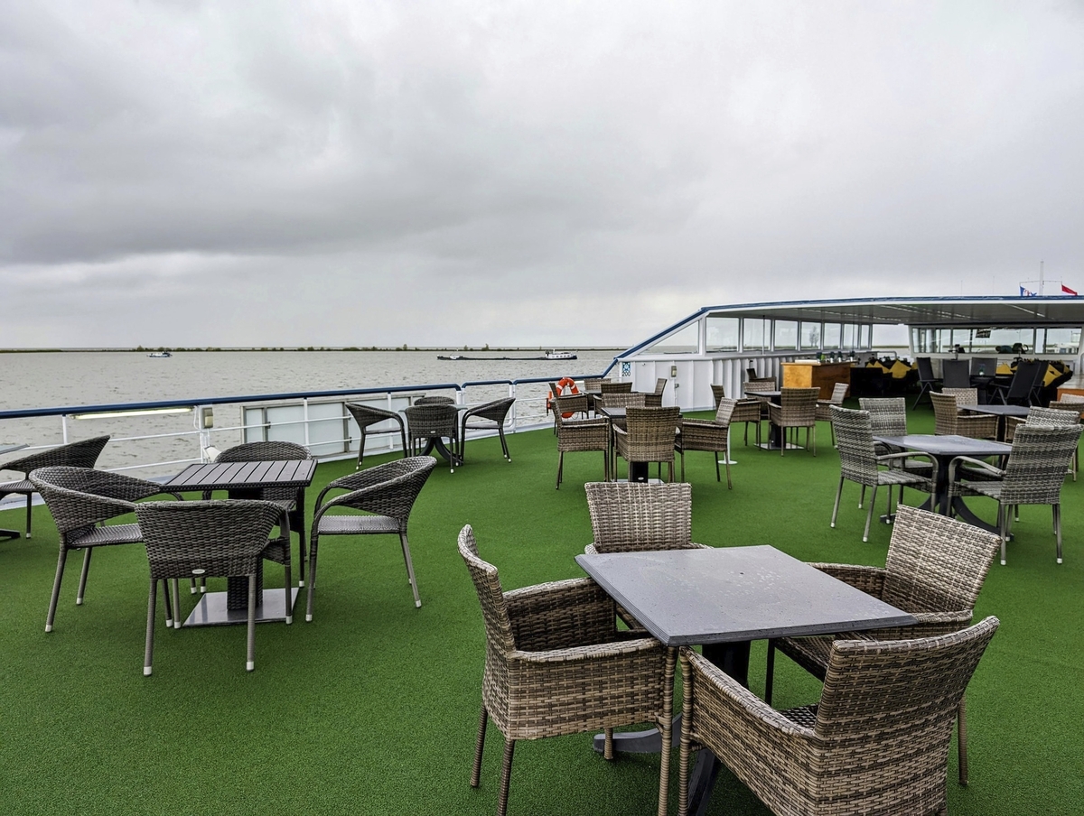 Sonnendeck eines Kreuzfahrtschiffs mit Tischen und Stühlen unter wolkigem Himmel.