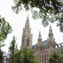 Wiener Rathaus, gotischer Stil, mit Bäumen im Vordergrund und österreichischen Fahnen.