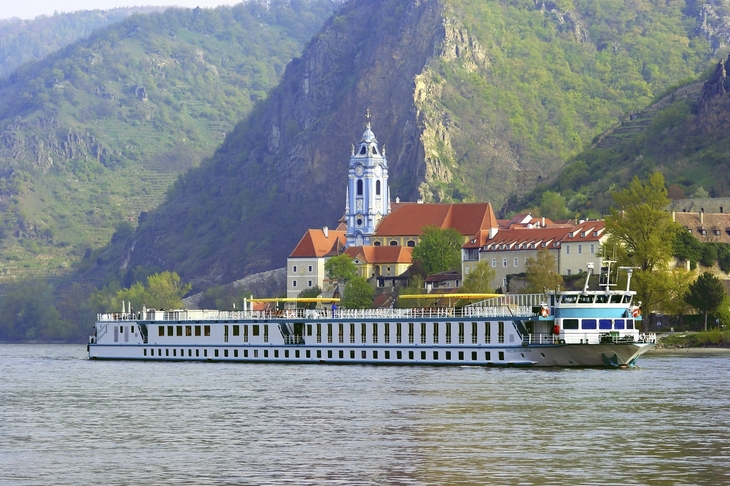 Flusskreuzfahrtschiff MS Prinzessin Katharina auf einem Fluss vor einer Berglandschaft.