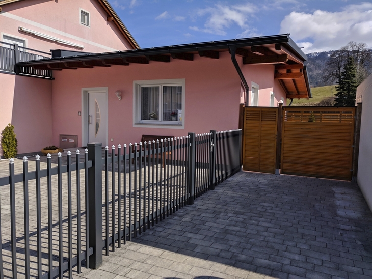Vorderansicht eines rosa Bungalows mit Zaun und Einfahrt im Vordergrund.