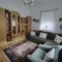 Wohnzimmer mit grüner Couch, Holzmöbeln und Teppich, weiße Wände und Lampe.