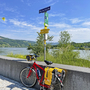 Rotes Fahrrad vor Donau und Radwegweiser unter blauem Himmel.
