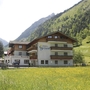 Hotelgebäude in bergiger Landschaft mit Wiesen und Wald im Hintergrund.