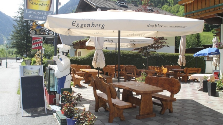 Terrasse eines Restaurants mit Holzmöbeln und großen Sonnenschirmen.