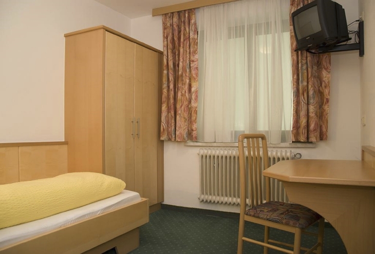 Einfach eingerichtetes Hotelzimmer mit Bett, Schreibtisch, Stuhl und Fernseher.