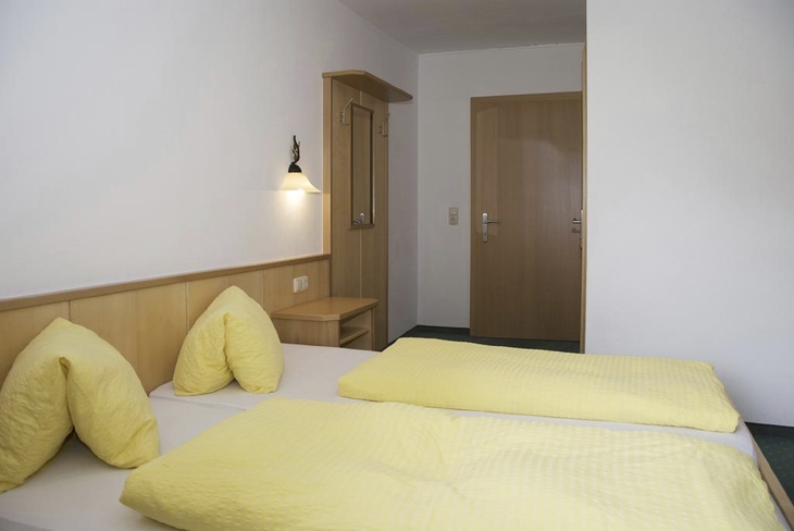 Hotelzimmer mit zwei Einzelbetten, hellem Holz und gelber Bettwäsche.