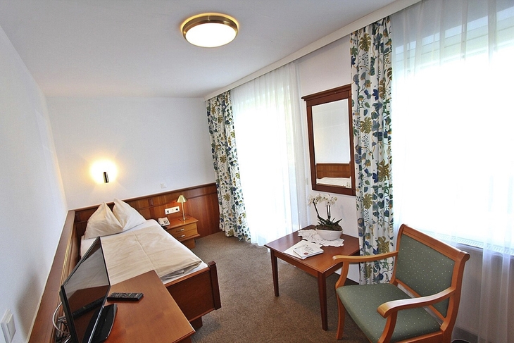 Einzelzimmer mit Bett, Tisch, Stuhl und Fenster mit Vorhängen im Landhotel Post Ebensee.