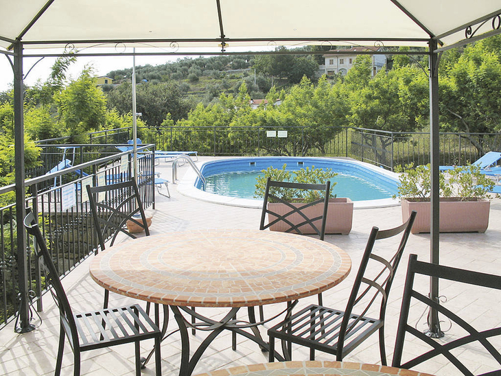 Terrasse mit Tisch und Stühlen vor einem Pool, umgeben von grüner Landschaft.