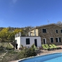 Steinhaus mit Terrasse, umgeben von Garten und Pool bei sonnigem Wetter.