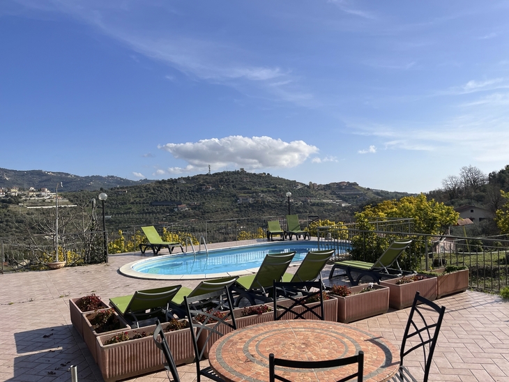 Terrasse mit Pool und Liegestühlen, Aussicht auf Hügel und blauen Himmel.