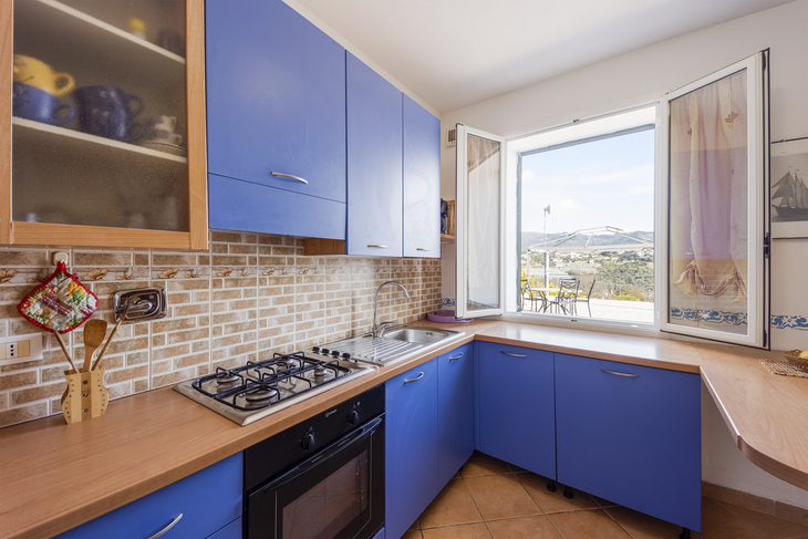 Küche mit blauen Schränken, Backofen und offenem Fenster mit Blick ins Freie.