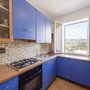 Küche mit blauen Schränken, Backofen und offenem Fenster mit Blick ins Freie.