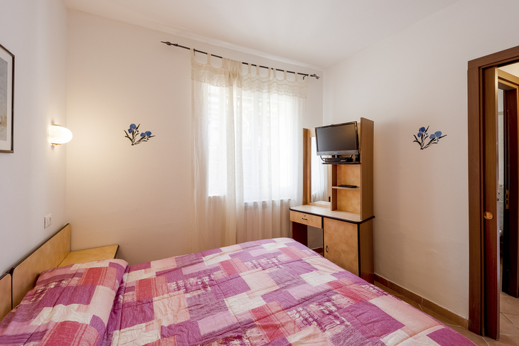 Schlafzimmer mit Doppelbett, TV und Fenster mit Vorhängen.