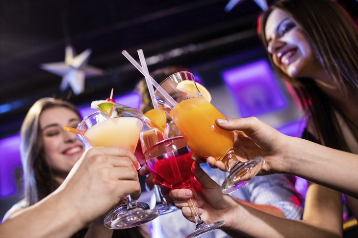 Menschen stoßen mit bunten Cocktails bei einer Party an.
