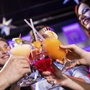 Menschen stoßen mit bunten Cocktails bei einer Party an.