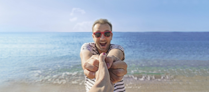 Mann lächelt am Ostseestrand und hält eine Hand.