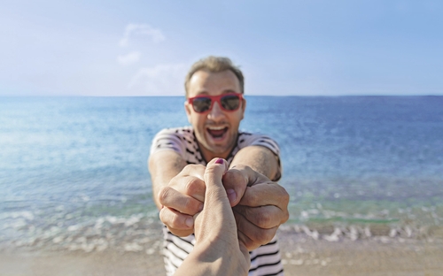 Mann lächelt am Ostseestrand und hält eine Hand.