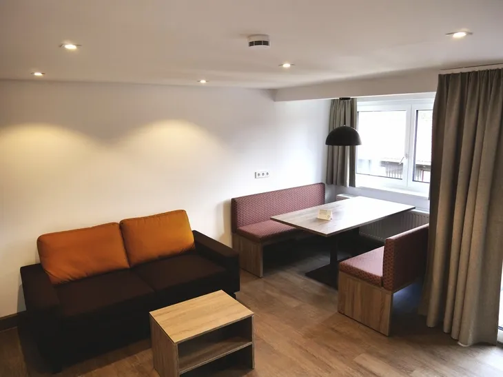 Wohnzimmer mit Sofa, Tisch, Eckbank und Fenster, moderne Beleuchtung.