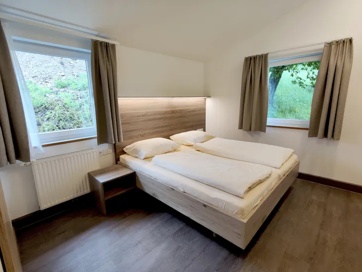 Renovierter Schlafraum mit Doppelbett und zwei Fenstern.