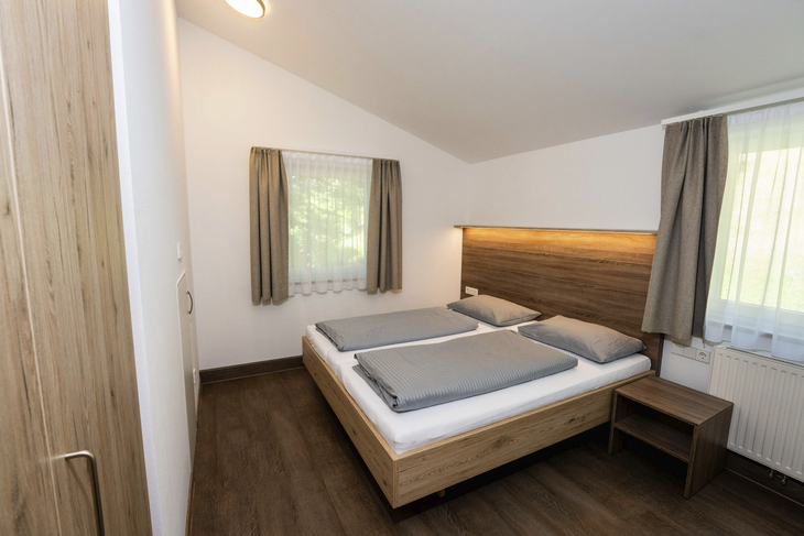 Gemütliches Schlafzimmer mit Doppelbett, Holzmöbeln und zwei Fenstern.